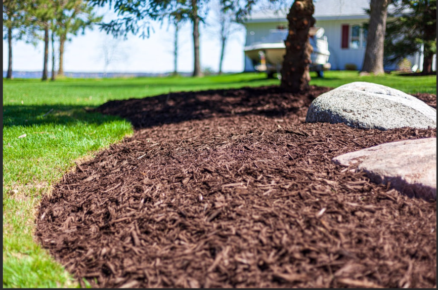 Mulching photo showing fresh dark mulch around a landscaped bed with stone edging.